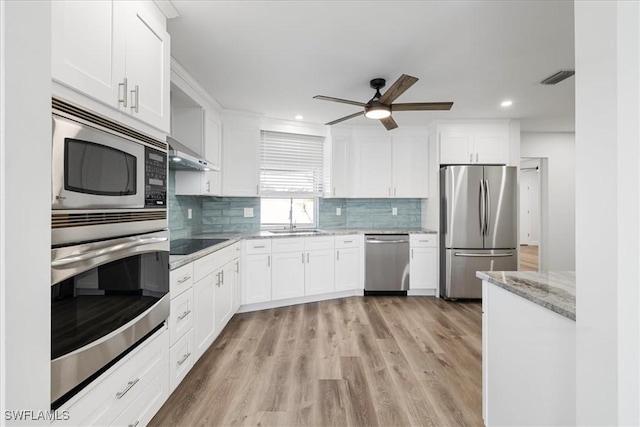 kitchen with light stone counters, stainless steel appliances, tasteful backsplash, white cabinets, and a sink