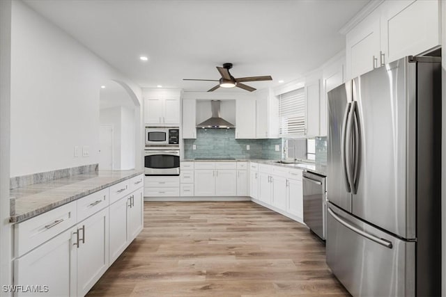 kitchen with stainless steel appliances, white cabinets, a sink, light stone countertops, and wall chimney exhaust hood