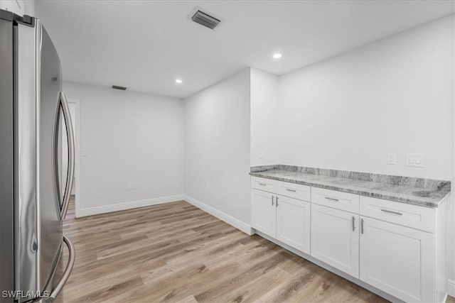 kitchen featuring light stone counters, visible vents, freestanding refrigerator, white cabinets, and light wood-type flooring