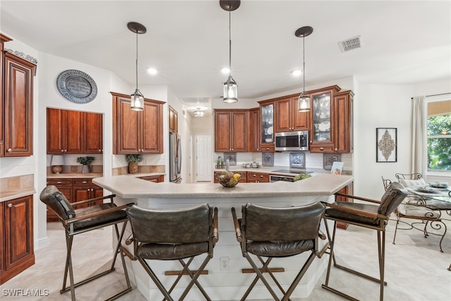 kitchen featuring light countertops, visible vents, hanging light fixtures, appliances with stainless steel finishes, and glass insert cabinets