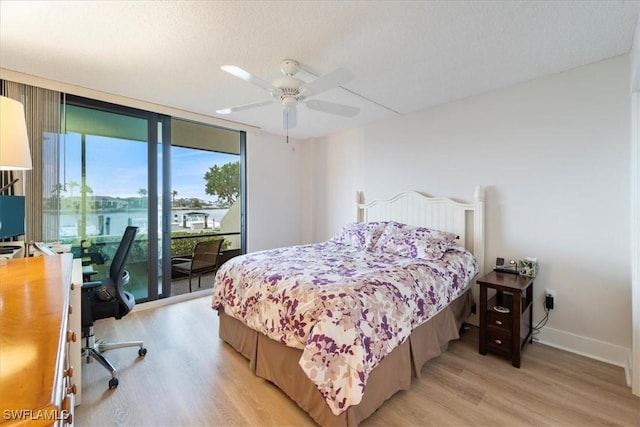 bedroom with a water view, light wood-type flooring, access to outside, expansive windows, and ceiling fan