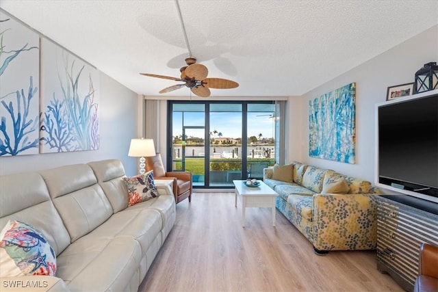 living room with ceiling fan, a wall of windows, a textured ceiling, and light wood-type flooring