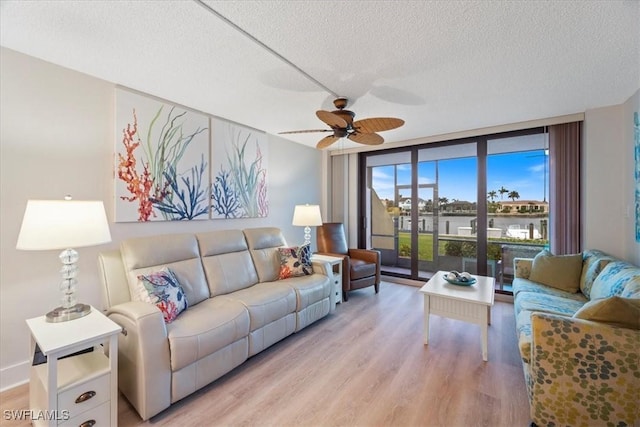 living room with ceiling fan, a wall of windows, a textured ceiling, and light wood-type flooring