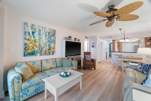 living room featuring ceiling fan with notable chandelier, wood-type flooring, and a textured ceiling