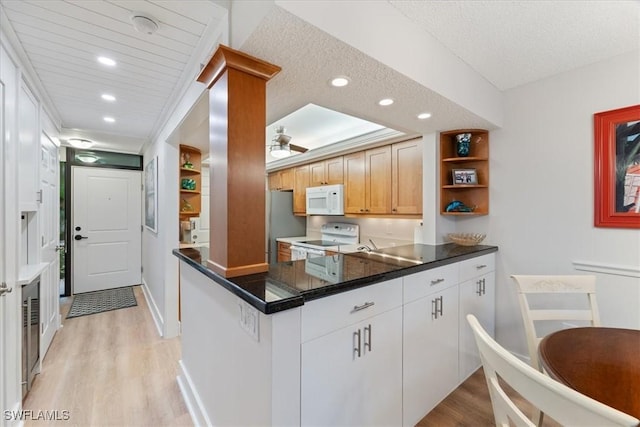 kitchen with white appliances, light hardwood / wood-style flooring, kitchen peninsula, ceiling fan, and white cabinets