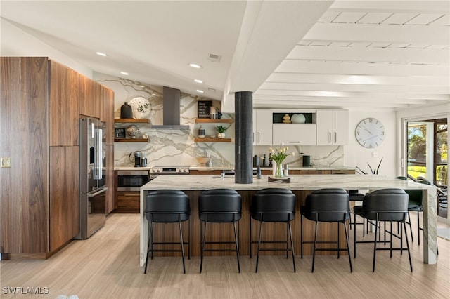 kitchen with appliances with stainless steel finishes, white cabinets, a kitchen bar, decorative backsplash, and wall chimney exhaust hood