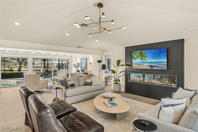 living room with a fireplace, light hardwood / wood-style floors, a chandelier, and vaulted ceiling