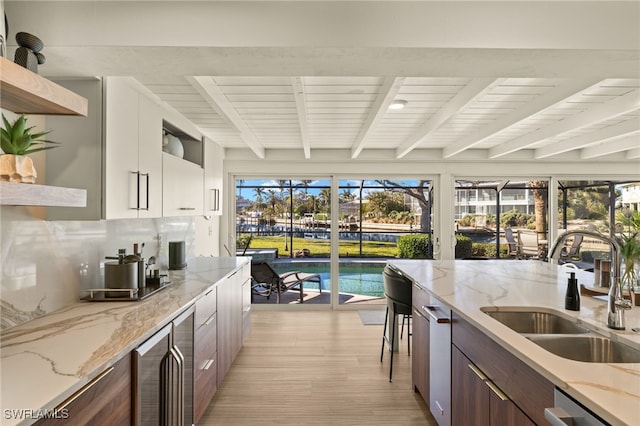 kitchen with sink, light stone counters, white cabinets, beverage cooler, and beamed ceiling