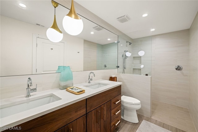 bathroom featuring a tile shower, vanity, toilet, and tile walls