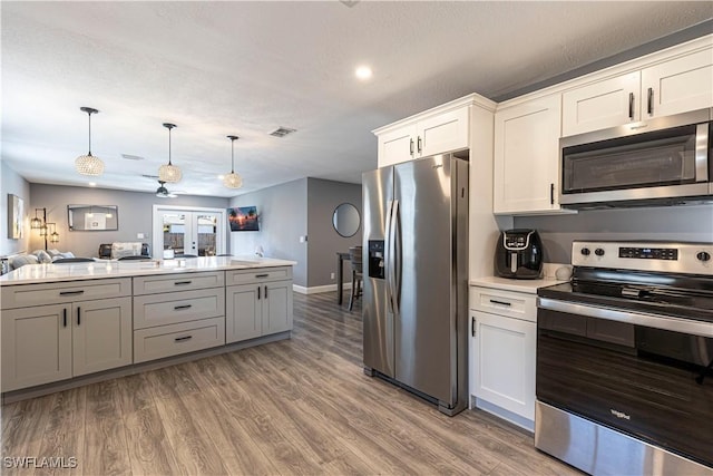 kitchen featuring pendant lighting, appliances with stainless steel finishes, white cabinetry, wood-type flooring, and french doors