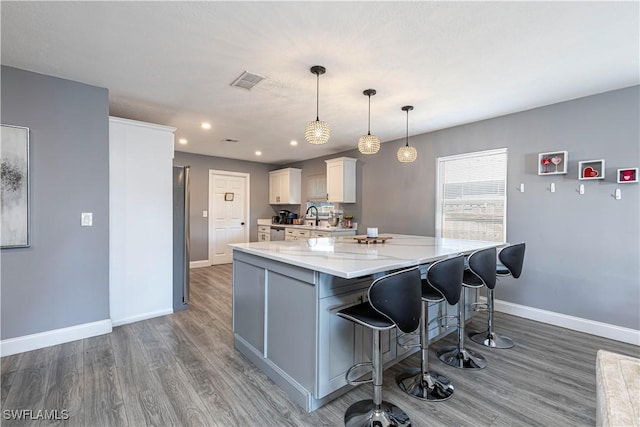 kitchen with a large island, hanging light fixtures, a kitchen breakfast bar, light stone counters, and wood-type flooring