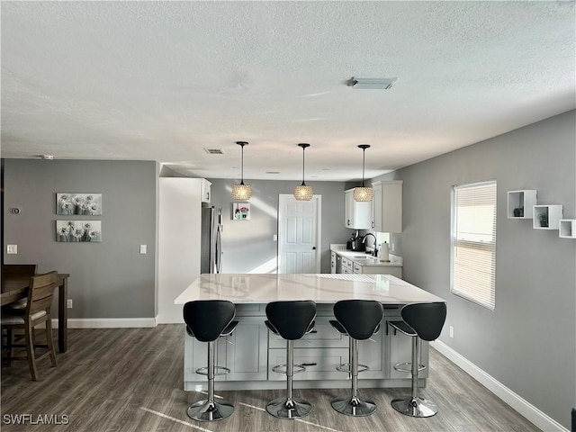 kitchen featuring dark wood-type flooring, light stone counters, stainless steel refrigerator, a kitchen island, and pendant lighting