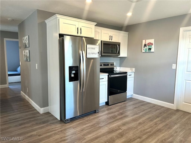 kitchen with stainless steel appliances, white cabinetry, and hardwood / wood-style flooring