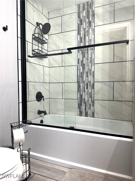 bathroom featuring hardwood / wood-style floors, toilet, and combined bath / shower with glass door