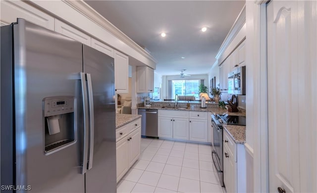 kitchen with appliances with stainless steel finishes, white cabinets, light tile patterned floors, light stone counters, and crown molding