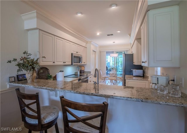 kitchen with light stone countertops, stainless steel appliances, kitchen peninsula, and white cabinets