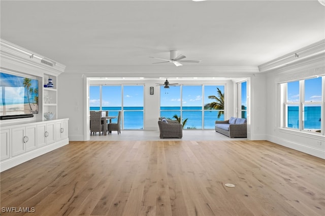 unfurnished living room with a water view, a healthy amount of sunlight, ornamental molding, and light wood-type flooring