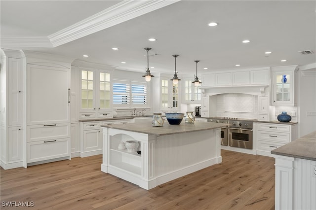 kitchen featuring white cabinetry, crown molding, decorative light fixtures, a kitchen island, and oven