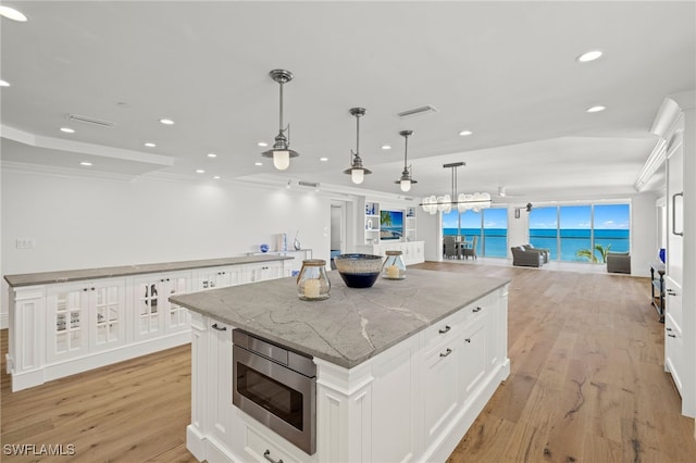 kitchen with pendant lighting, stainless steel microwave, a large island, and white cabinets