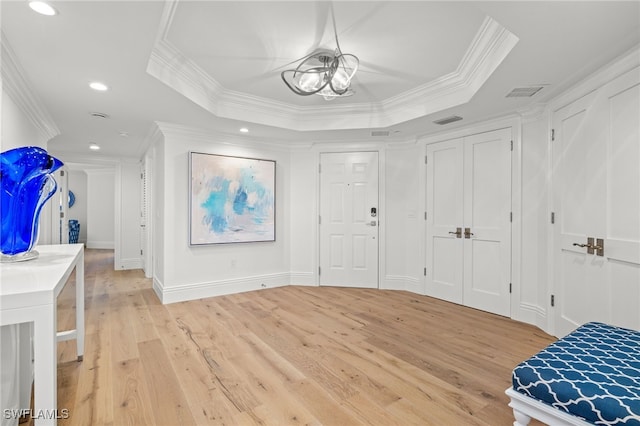 entrance foyer featuring crown molding, a tray ceiling, light hardwood / wood-style flooring, and an inviting chandelier