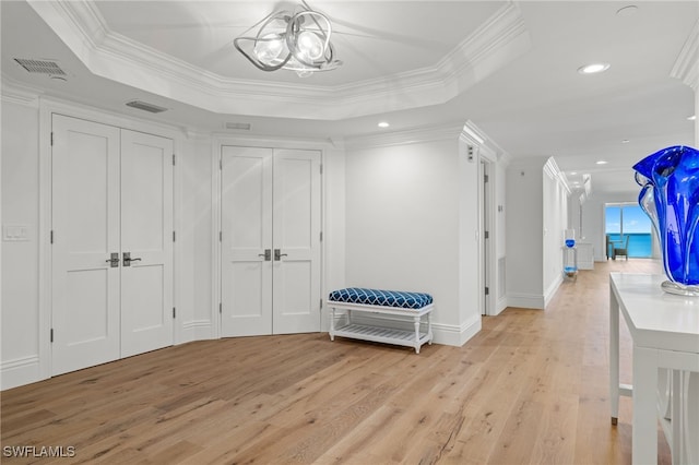 hall featuring crown molding, a tray ceiling, an inviting chandelier, and light wood-type flooring