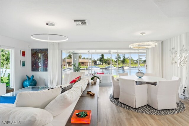 dining room featuring an inviting chandelier, a wealth of natural light, light hardwood / wood-style floors, and a water view