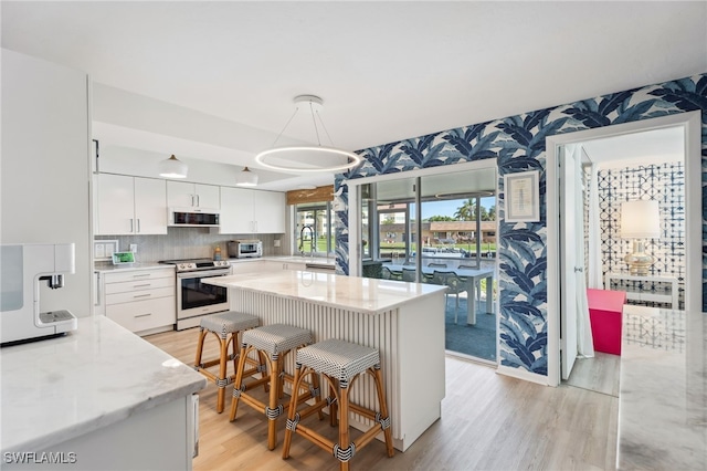 kitchen with light stone countertops, stainless steel electric range, decorative light fixtures, and white cabinets