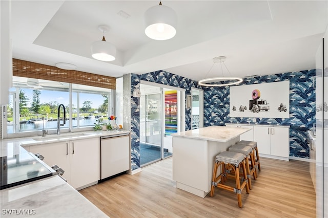 kitchen with hanging light fixtures, white cabinetry, sink, and dishwashing machine