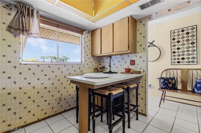 kitchen with light tile patterned floors, a breakfast bar, visible vents, light countertops, and wallpapered walls