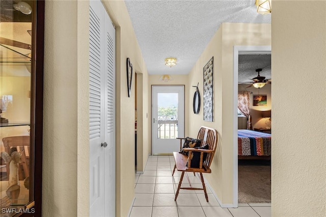 hall with a textured ceiling, light tile patterned flooring, and baseboards