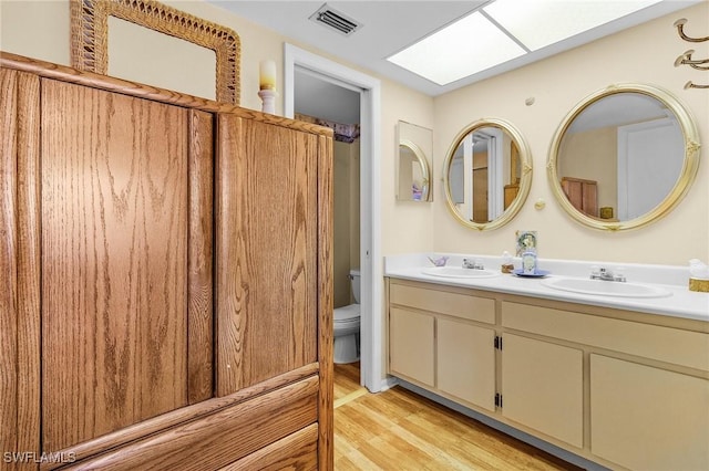 bathroom featuring a skylight, a sink, toilet, and double vanity