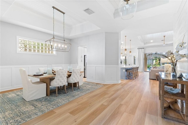 dining area featuring an inviting chandelier, light wood-type flooring, and a tray ceiling