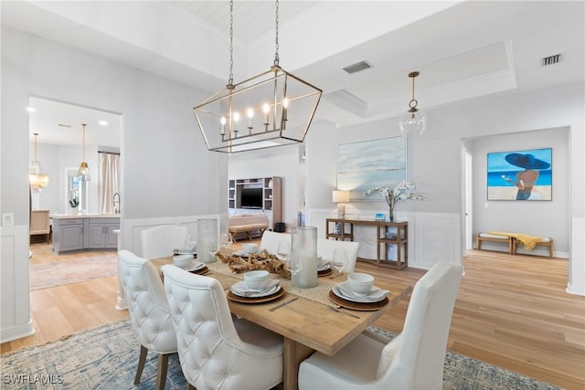 dining room with ornamental molding, a tray ceiling, an inviting chandelier, and light hardwood / wood-style flooring