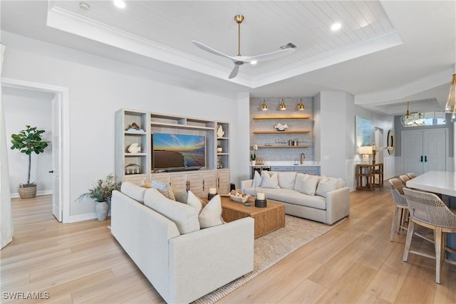 living room featuring ceiling fan, ornamental molding, a raised ceiling, and light wood-type flooring