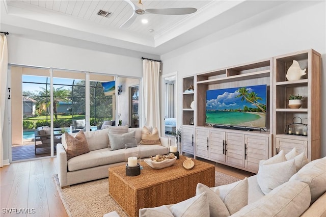 living room with ceiling fan, a raised ceiling, crown molding, wooden ceiling, and light wood-type flooring