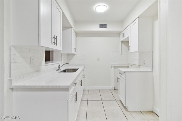 kitchen featuring sink, light tile patterned floors, white cabinetry, tasteful backsplash, and light stone countertops