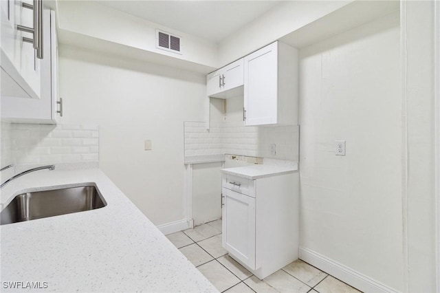 kitchen with light tile patterned flooring, sink, white cabinetry, light stone counters, and tasteful backsplash