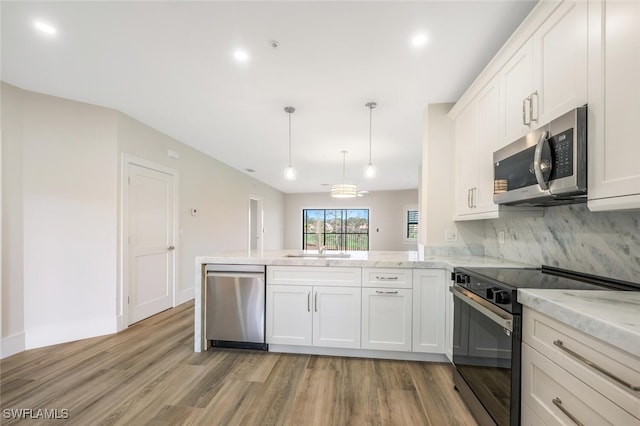 kitchen with hanging light fixtures, light wood-type flooring, appliances with stainless steel finishes, kitchen peninsula, and white cabinets