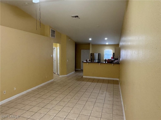 interior space with light tile patterned floors, stainless steel refrigerator, and kitchen peninsula