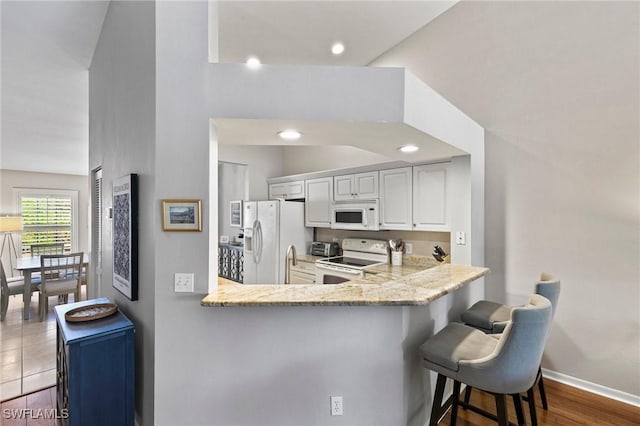 kitchen with white cabinetry, white appliances, a kitchen breakfast bar, and kitchen peninsula