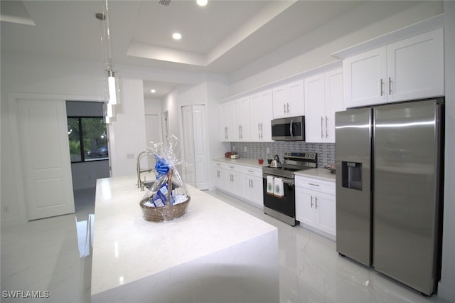 kitchen with decorative light fixtures, stainless steel appliances, white cabinets, and a center island with sink