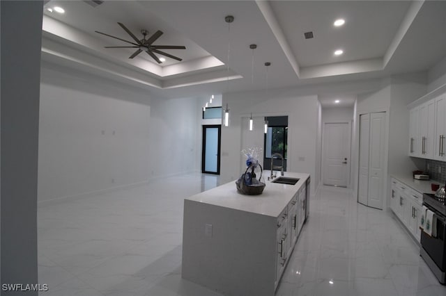 kitchen with sink, white cabinetry, hanging light fixtures, an island with sink, and a raised ceiling