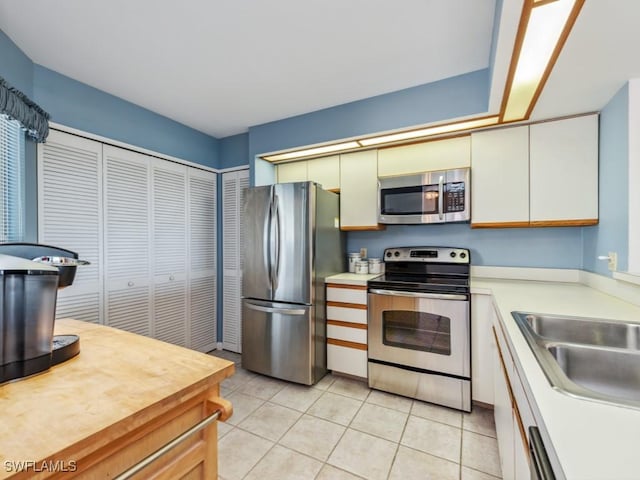 kitchen featuring light tile patterned flooring, appliances with stainless steel finishes, sink, and white cabinets