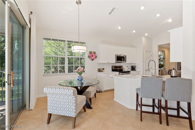 kitchen with pendant lighting, a breakfast bar area, appliances with stainless steel finishes, white cabinetry, and light tile patterned flooring