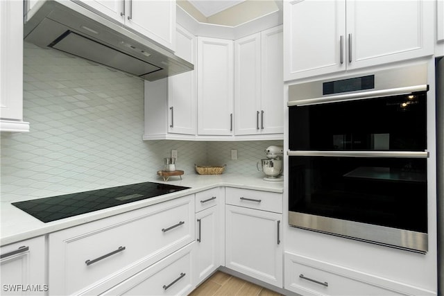 kitchen with white cabinetry, black electric stovetop, double oven, and wall chimney range hood