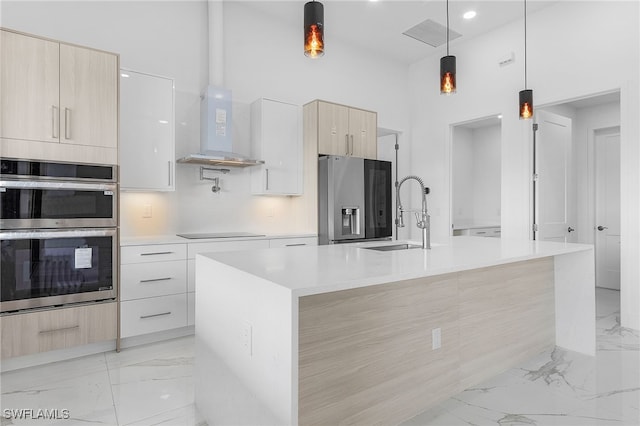 kitchen with sink, a kitchen island with sink, range hood, stainless steel appliances, and decorative light fixtures