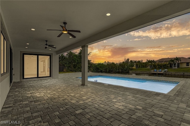 pool at dusk featuring ceiling fan and a patio