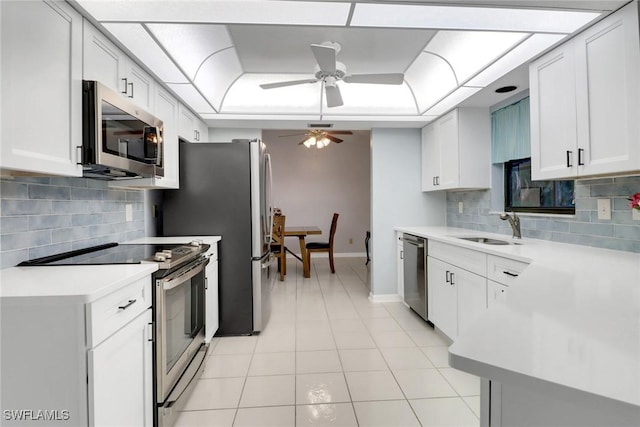 kitchen with sink, light tile patterned floors, appliances with stainless steel finishes, white cabinetry, and a raised ceiling