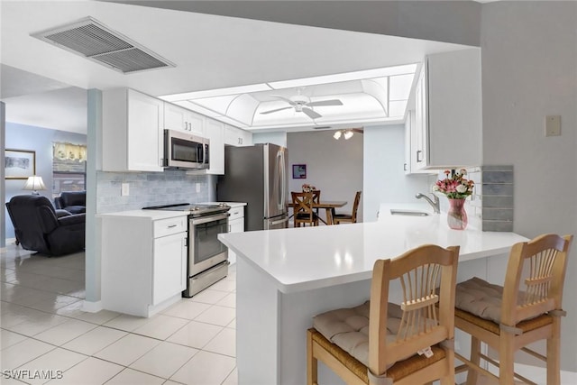 kitchen featuring a breakfast bar area, appliances with stainless steel finishes, kitchen peninsula, ceiling fan, and white cabinets