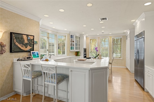 kitchen with a breakfast bar, white cabinetry, built in refrigerator, ornamental molding, and light hardwood / wood-style flooring